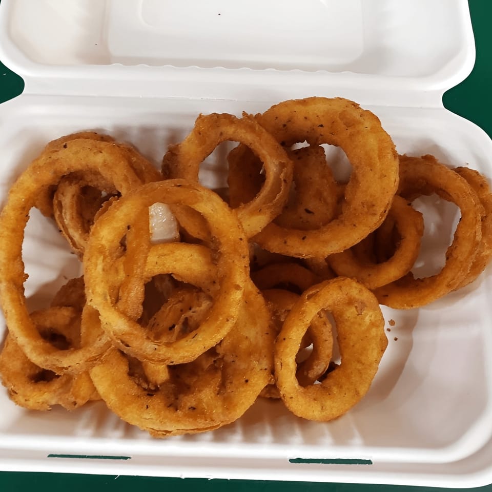 Golden-brown, crispy onion rings are piled high in a white takeout container from TNT Takeout.