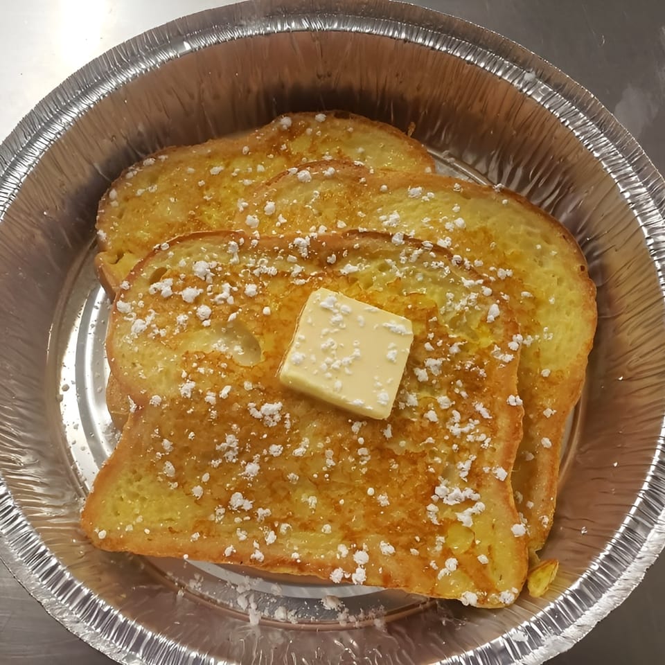 Three slices of French toast with powdered sugar and a pat of butter in a foil takeout container.