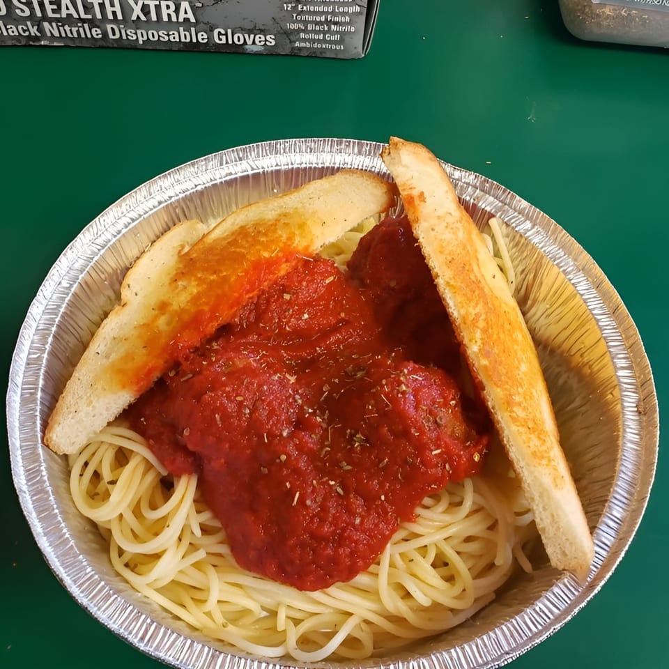Spaghetti with red sauce and two pieces of garlic bread in a foil takeout container.