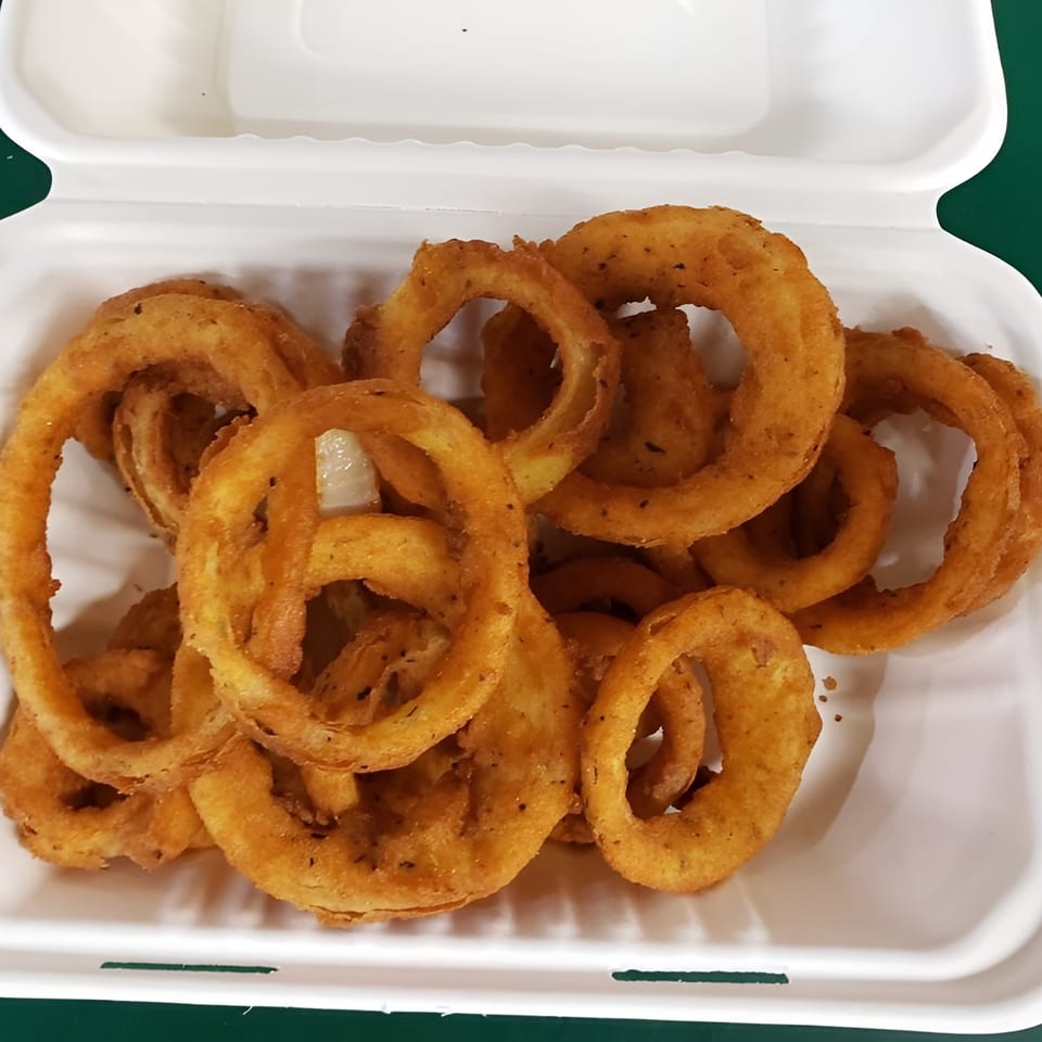 A white takeout container filled with golden-brown, crispy onion rings from TNT Takeout.