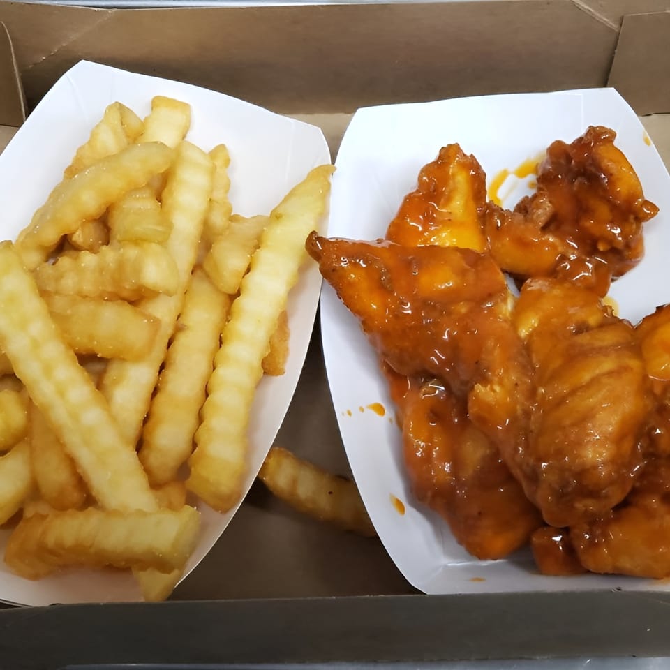 TNT Takeout's crinkle-cut fries and saucy boneless wings in white paper trays.