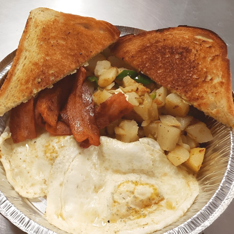 TNT Takeout breakfast with fried eggs, bacon, home fries, and toast in a foil container.